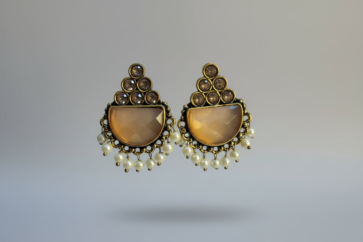 Gold and pearl earrings held by a hand with KAYAN branding in the background.